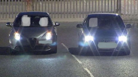 Two cars side by side in a road with their drivers' faces blacked out