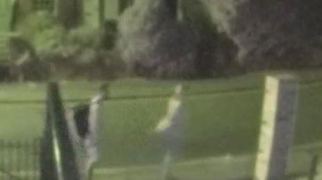 A man in a light coloured top and shorts, carrying a black rucksack, is picked up on CCTV walking down a residential street at night. He is with a woman dressed in light clothing with blond hair. They have a small dog. 