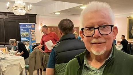 Ian Nightingale, who is wearing a green jacket and shirt and has black glasses, standing in a room where free PSA testing is taking place.