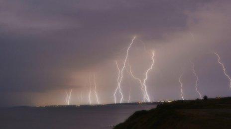 Multiple lines of lightning come of out grey orange clouds and down to the ground