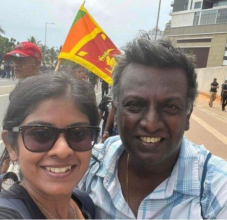 Dinithika and her father smile at protests in Colombo, in front of a Sri Lankan flag