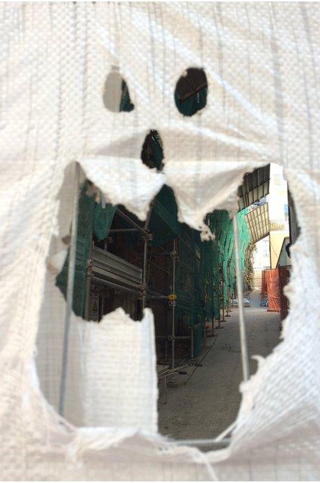 A face cut out of a builder's sheet exposes a ruined street in L'Aquila, September 2016