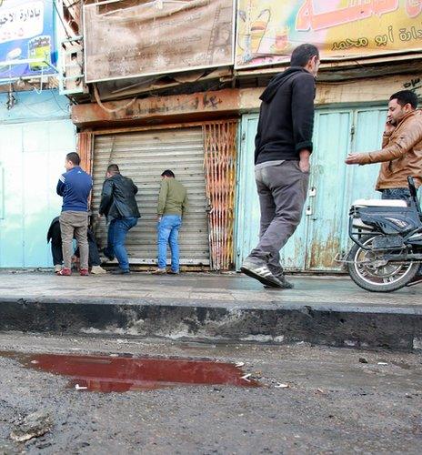 Men pass a bloodstained puddle on Tayaran Square, Baghdad, 15 January