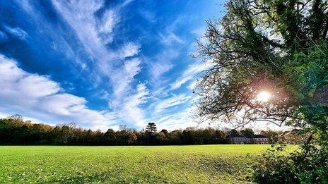 Blue skies with stretches of white cloud over green field