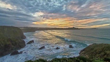 The sun setting over the sea at Porth, Cornwall, with yellow and blue sky reflected in the blue waterl