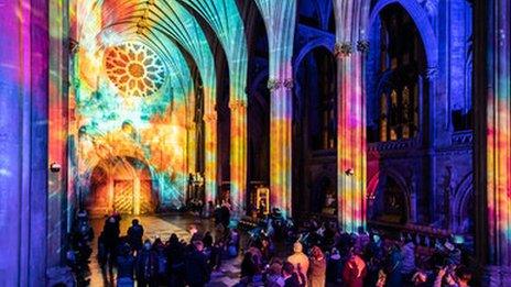 A photo of the colourful projected interior of the cathedral whilst the audience observe the walls.