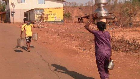 A man and a woman carry water up a dust road.