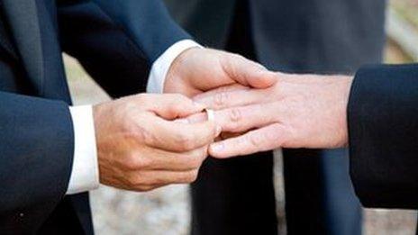 One groom placing a wedding ring on another groom's finger