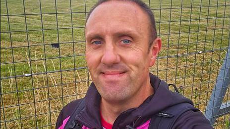 Man smiling with fence and grass behind.