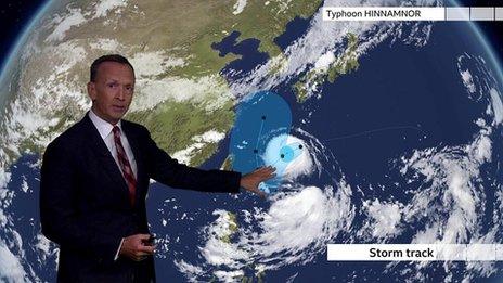 Nick Miller stands in front of a weather map showing the storm track for Typhoon Hinnamnor.