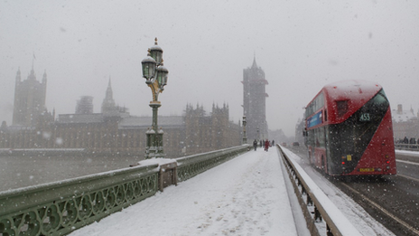 Snow covered Westminster bridge with House of Parliament just visible in heavy snow with a red London bus.