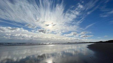 Hazy sun behind wispy cloud reflected in still water