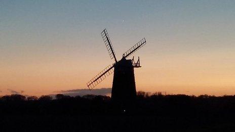 A windmill is in silhouette against the sky which has an orange layer across the horizon