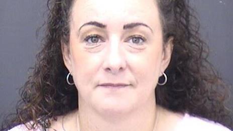 A custody photo of Emma Charlotte Amey, a woman with long dark curly hair and wearing small hoop earrings.