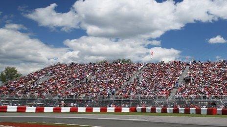 Spectators sit by the F1 track in Montreal. Blue skies and white clouds are overhead.