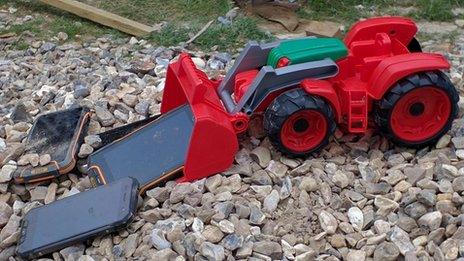 phones on toy digger on pile of stones