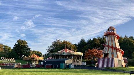 A blue sky sets the backdrop for a fun fair with an old fashioned red and white helter skelter to the right