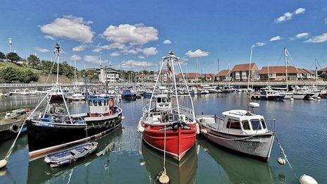 Colourful boats in a bay with houses behind and blue sky and fluffy white clouds overhead.