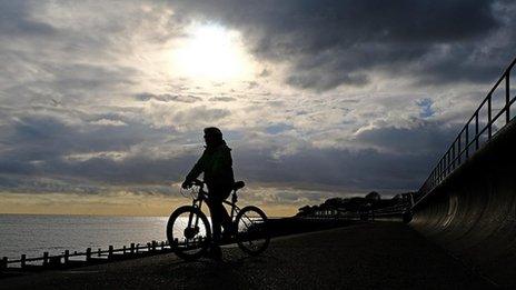 A cyclist is seen in silhouette against the setting sun in a cloudy sky over a silvery sea