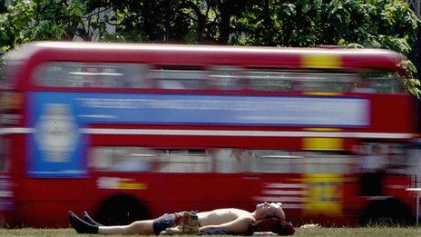 Man lying on the ground with a red London bus going past in the background