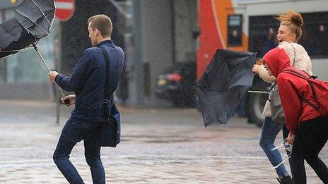 A man on the left and a woman on the right struggle with umbrellas turning inside out in a gusty storm