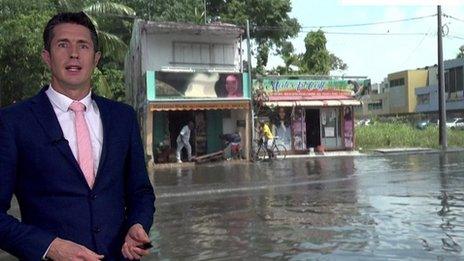 Chris Fawkes stands in front of an image of a flooded road in Guadeloupe