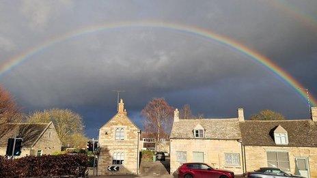 A rainbow, set in a dark cloudy sky, arcs aross the top of a row of houses