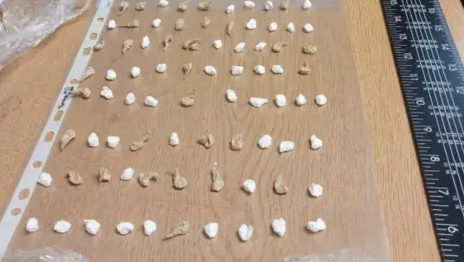 The drug wraps are small brown and white packages that are laid out in rows on a wooden surface. There is a ruler on the right-hand edge of the surface.