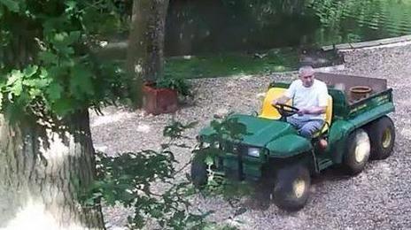 John Palmer in a white t-shirt is driving a green ride-on lawnmower on the gravel of his garden on a sunny day. A time code on the picture reads: 24-06-2015. Wed. 16:23:42.
