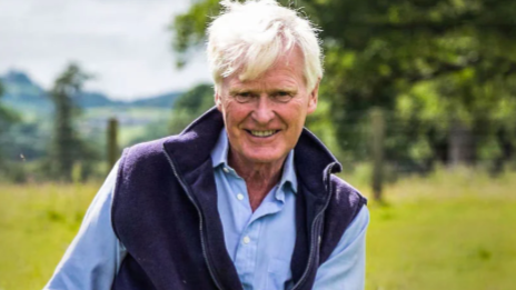 A man with white hair, wearing a blue jacket and light blue shirt