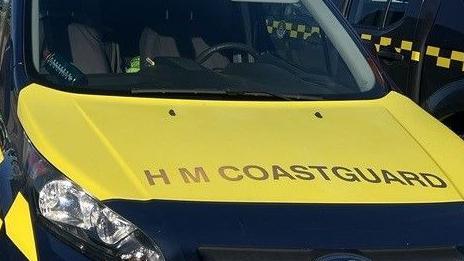 The front of a HM Coastguard vehicle. There is a yellow section with the words 'HM COASTGUARD' and underneath is it dark blue.