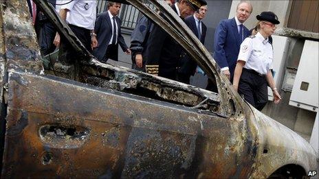 Interior Minister Brice Hortefeux (second from right) passes a charred car in Grenoble, 17 July