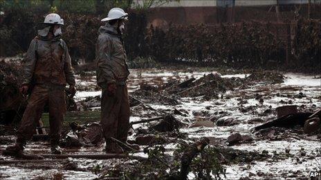 Hungarian firefighters, wearing protective gear, survey a yard flooded by toxic mud in the village of Kolontar, Hungary, Thursday, Oct. 7, 2010.