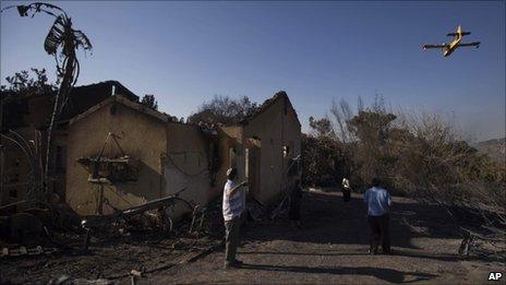 As a firefighting plane flies over, members of the Cohen family walk next to the remains of their house, burnt in the fire, in the youth village (boarding school) of Yemin Orde, near the northern city of Haifa, Israel, Sunday, Dec. 5, 2010