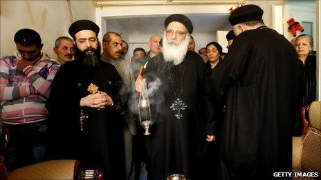 Relatives of Egyptian Copt Fawzi Bakhit who was killed in the New Year's Day church bombing in Alexandria gather behind a priest blessing Mr Bakhit's home with incense, 3 January 2011