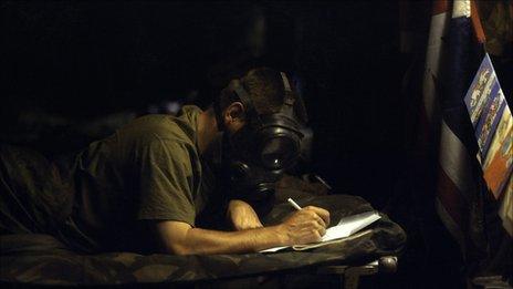 A soldier wearing a gas masks writes a letter during the Gulf War, 1991