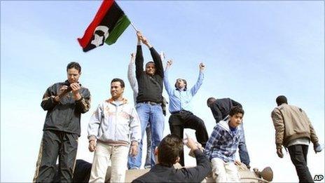 Residents stand on a tank holding a pre-Gaddafi era national flag inside a security forces compound in Benghazi, Libya on Monday, Feb. 21, 2011