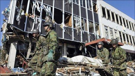 Japanese soldiers walk past a damaged building in the city of Rikuzentakada, Japan, on 12 March, 2011