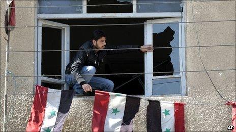 A Syrian security man, sets Syrian flags through a broken window of an office destroyed by Syrian anti-government protesters, in the southern city of Daraa, Syria