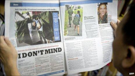 Photograph taken on 30 March 2011 shows a reader of a local newspaper looking at the photo of a maid carrying a soldier's bag for him