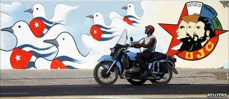 A man rides his motorcycle past a freshly painted mural by the Union of Young Communists, in Havana April 15, 2011