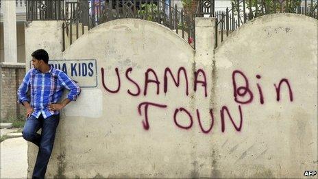 A Pakistani man leans against a wall bearing the graffiti "Osama Bin Town" near the hideout house of slain Al-Qaeda leader Osama bin Laden