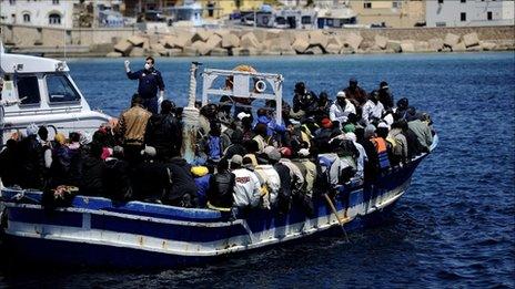 A policemen escorts a boat with more 200 people aboard arriving at Lampedusa from Libya on 9 April 2011