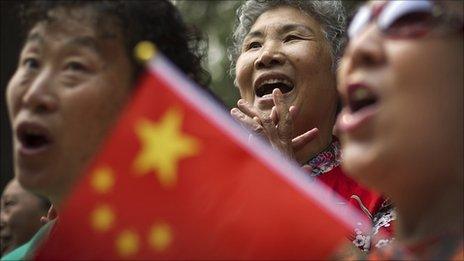 A Chinese woman waves a national flag while singing patriotic songs to celebrate the up-coming 90th anniversary of the founding of CCP