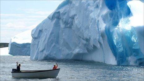 Two people in a boat moving past an iceberg