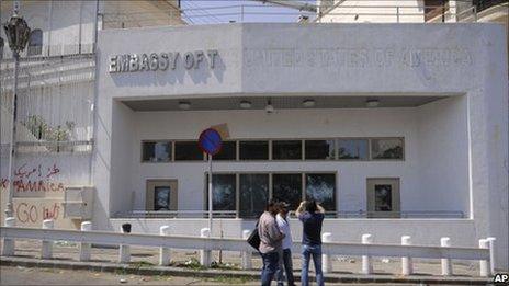 Men checks the damaged US embassy in Syria after a pro-government crowd attacked it, 11 July.