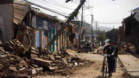 A man pushing a bicycle through a damaged street after an earthquake struck Chile in 2010.