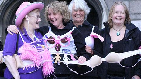 Women stand in front of chain of bras