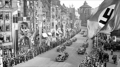 Adolf Hitler salutes supporters from a car as he passes through Nuremberg, 5 September 1938