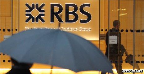 Man with umbrella walks past an RBS bank